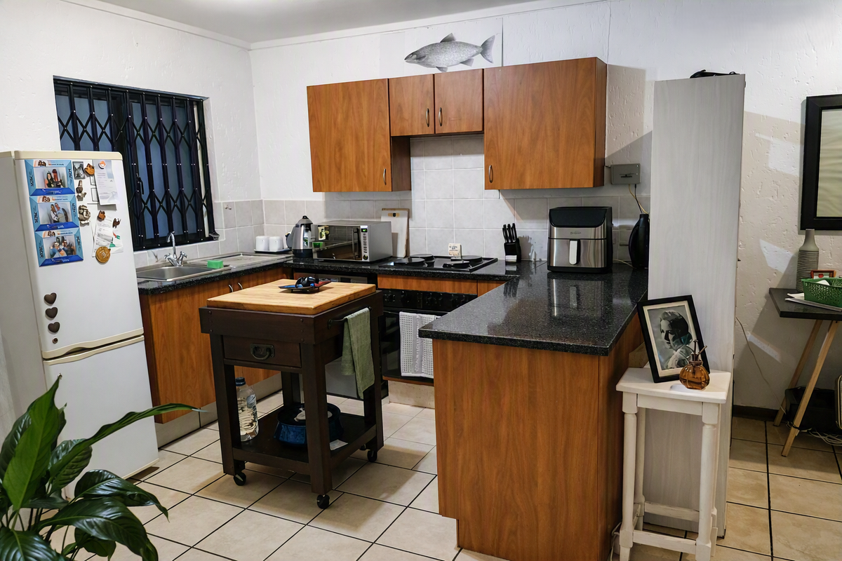 A functional kitchen featuring wood-look laminate cabinetry, dark granite countertops, ceramic tile backsplash, and tiled flooring with a window security gate.
