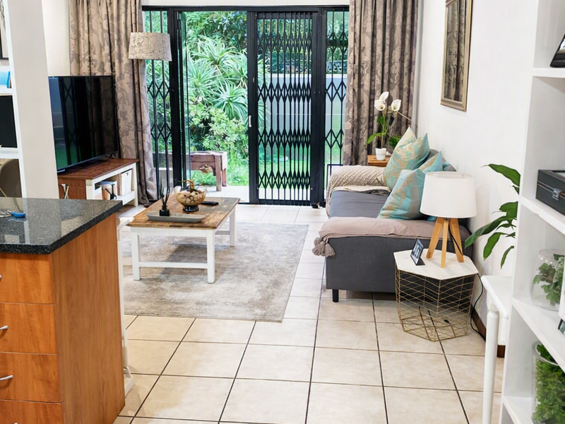 Open-plan living area featuring tiled flooring, granite kitchen countertops, and sliding glass doors leading to a private garden space.