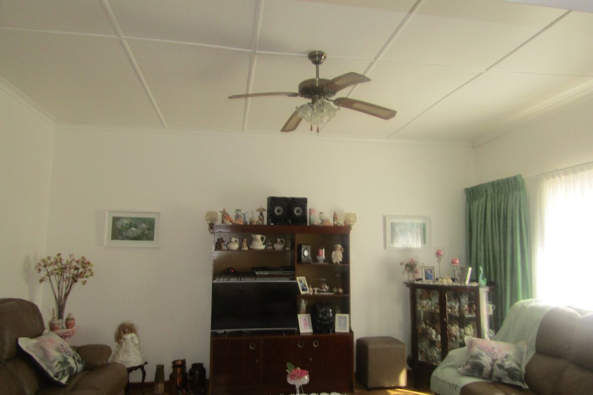 A living room featuring hardwood flooring, a ceiling fan, and a tiled ceiling finish.