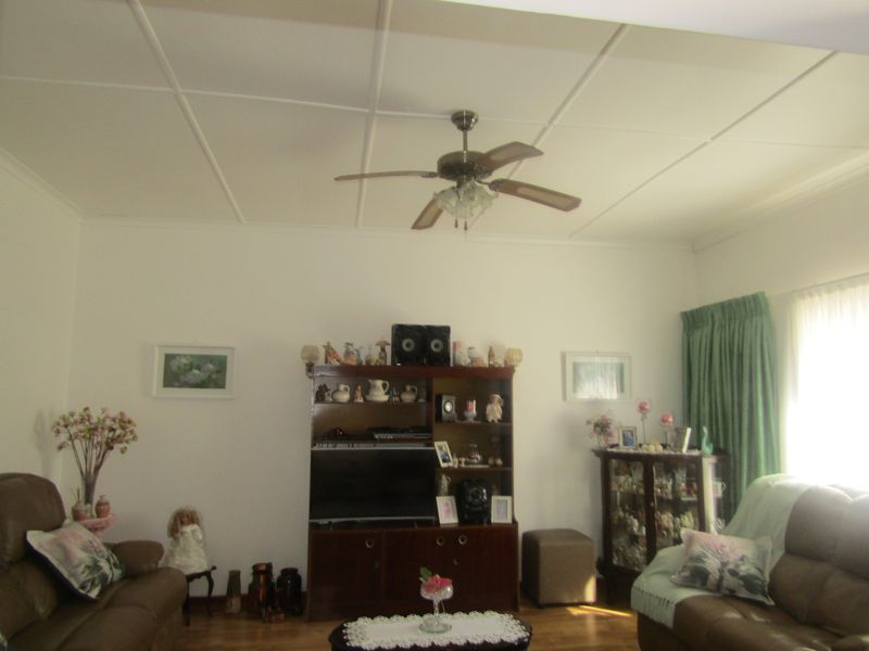 A living room featuring hardwood flooring, a ceiling fan, and a tiled ceiling finish.