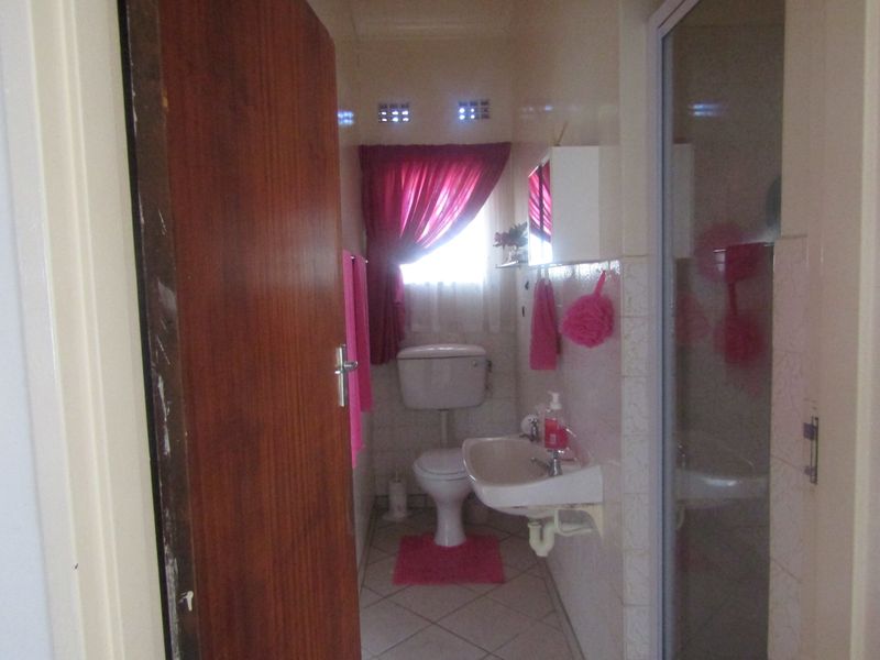A compact bathroom featuring a wall-mounted basin, toilet, and a shower enclosure with tiled finishes throughout.