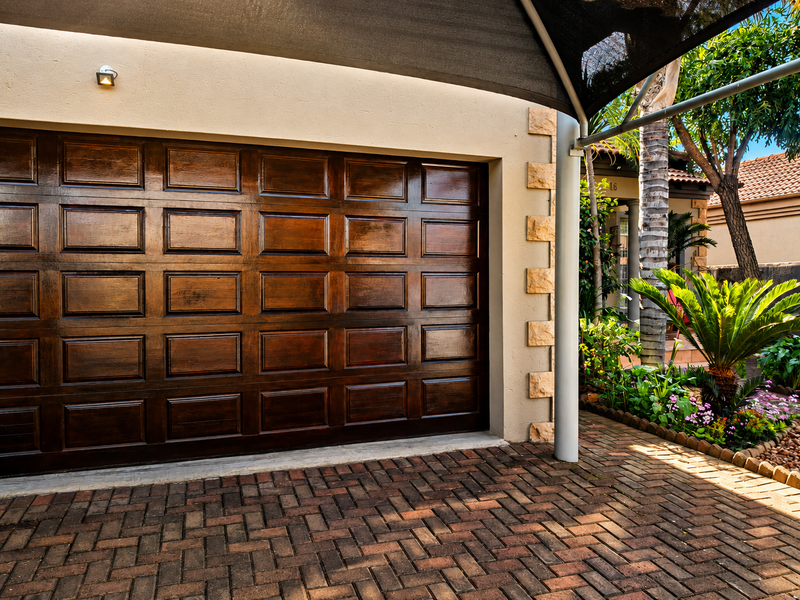 A well-maintained garage exterior featuring a polished wooden sectional door, paved driveway, and decorative stone cladding accents.