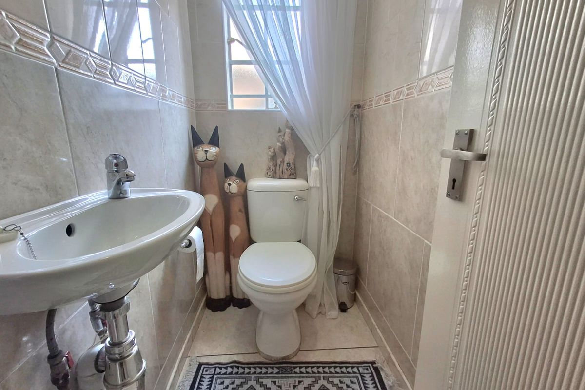 A compact guest bathroom featuring neutral ceramic wall and floor tiles, a pedestal basin with chrome fixtures, and a standard toilet.