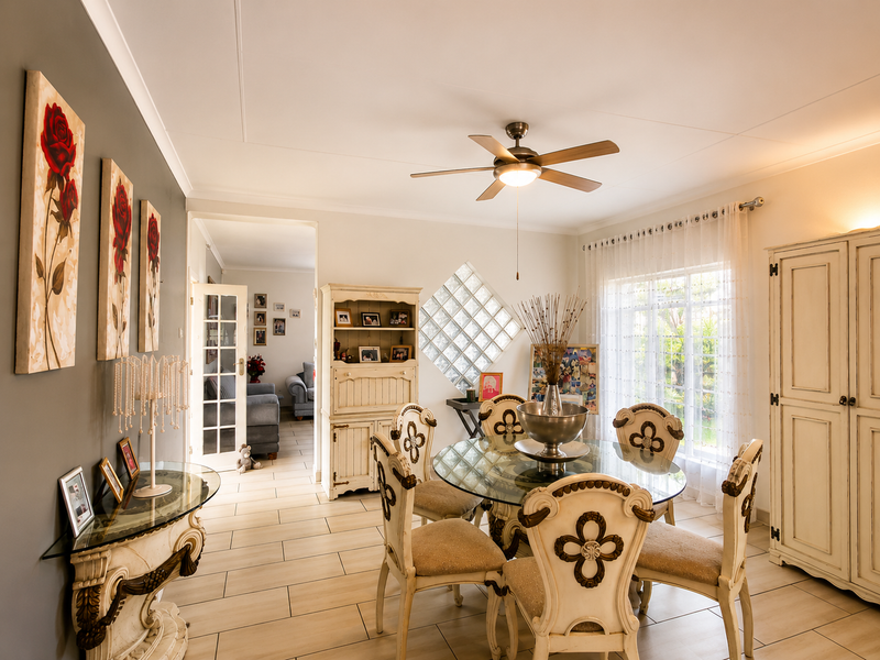 A well-lit dining room featuring tiled flooring, a central ceiling fan, and a decorative glass block window, providing a bright and functional space.