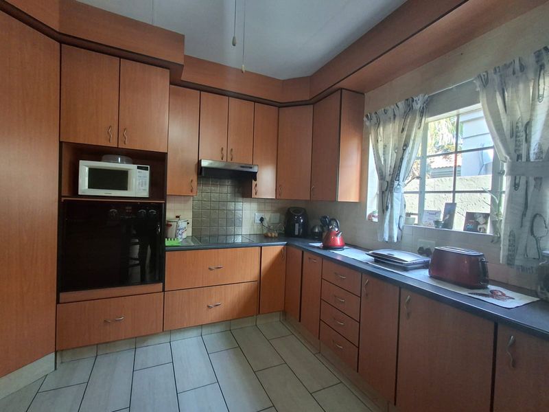 A functional kitchen featuring wood-look laminate cabinetry, built-in oven, extractor fan, and tiled flooring with a tiled splashback.
