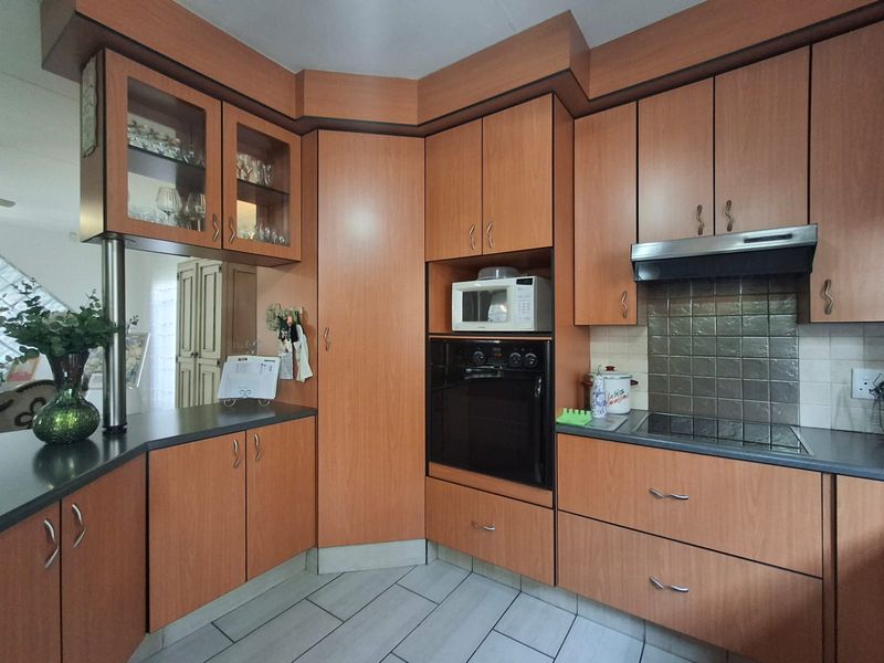 A functional kitchen featuring wood-look cabinetry, built-in oven, electric hob with extractor fan, and tiled flooring.