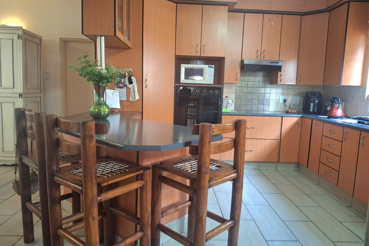 A functional kitchen featuring wood-look laminate cabinetry, a built-in oven, extractor fan, and a central breakfast bar with tiled flooring throughout.