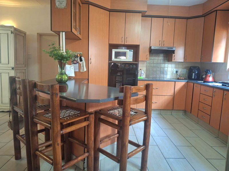 A functional kitchen featuring wood-look laminate cabinetry, a built-in oven, extractor fan, and a central breakfast bar with tiled flooring throughout.