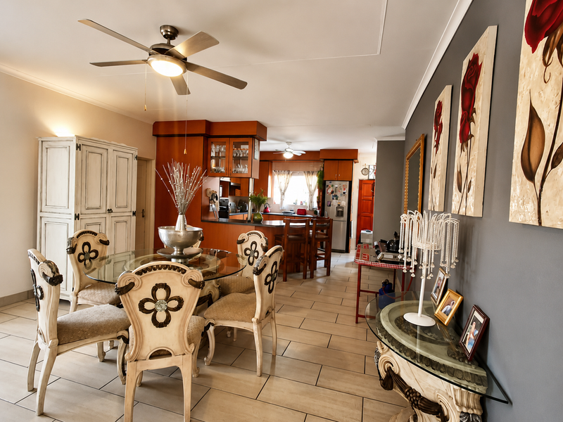 An open-plan living and dining area featuring tiled floors, a central ceiling fan, and a functional kitchen with wooden cabinetry and an island.