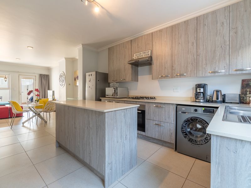 Open-plan kitchen and living area featuring modern wood-look cabinetry, stone countertops, integrated appliances, and tiled flooring leading to an outdoor patio.