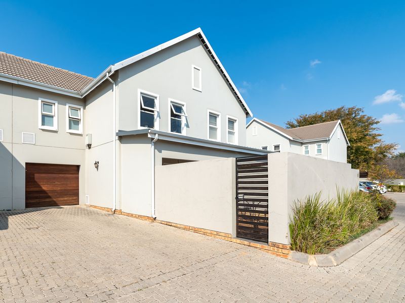 Front exterior view of a modern townhouse featuring a paved driveway, timber garage door, and a private gated entrance.