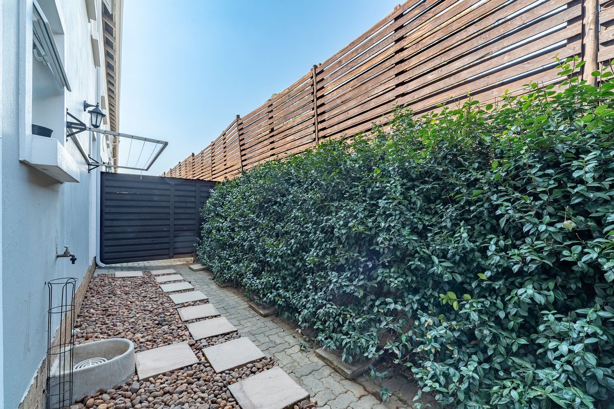 A private rear courtyard featuring a paved walkway, pebble landscaping, and tall wooden perimeter fencing with established hedge screening.