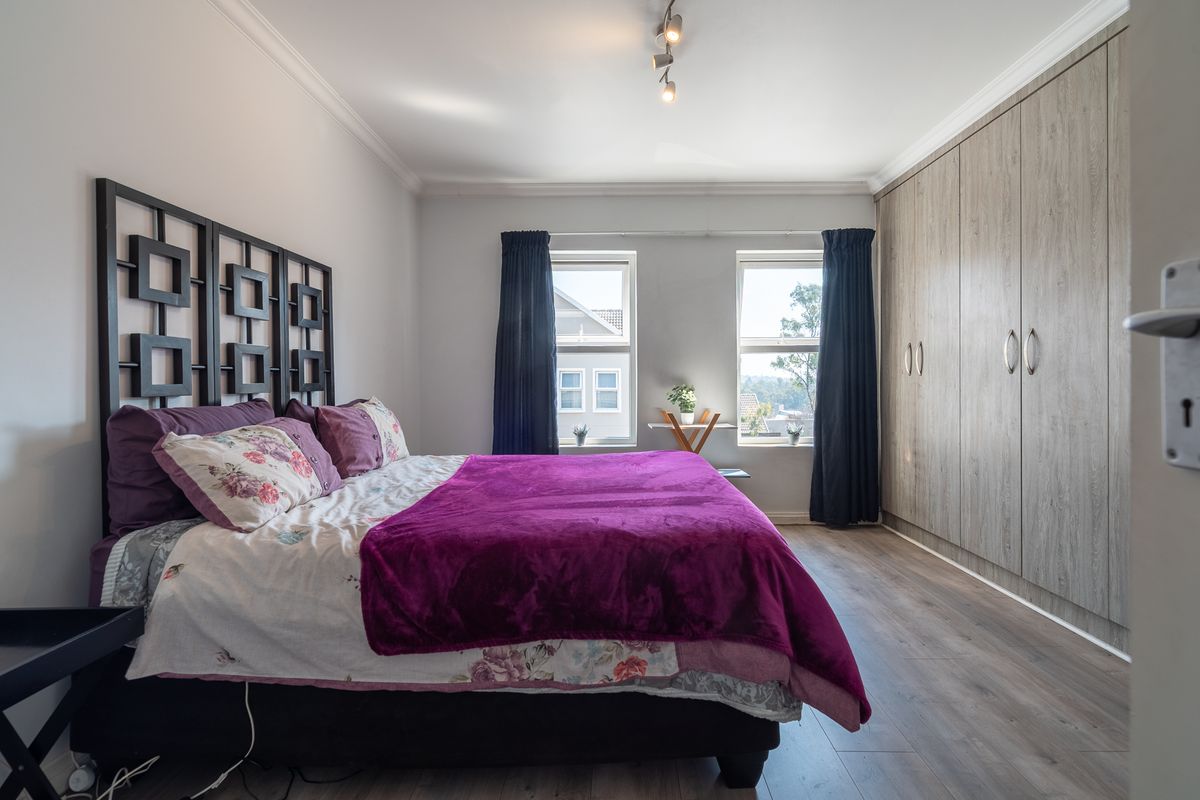 A well-maintained bedroom featuring laminate flooring, built-in cupboards, and dual windows providing natural light.