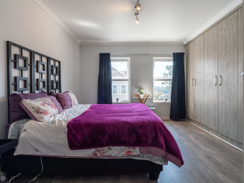 A well-maintained bedroom featuring laminate flooring, built-in cupboards, and dual windows providing natural light.