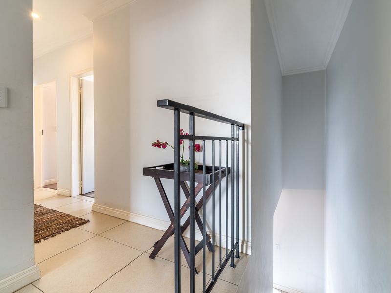 A bright, tiled hallway featuring a metal stair railing and clean, neutral wall finishes leading to adjacent rooms.