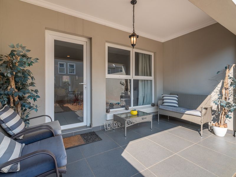 A covered patio area featuring dark tiled flooring, a pendant light fixture, and direct access to the interior through a glass-paneled door.