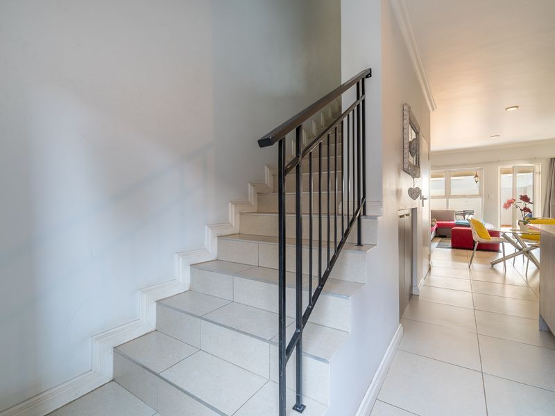 A bright hallway featuring a tiled staircase with a black metal balustrade, leading into an open-plan living area with neutral floor tiles.