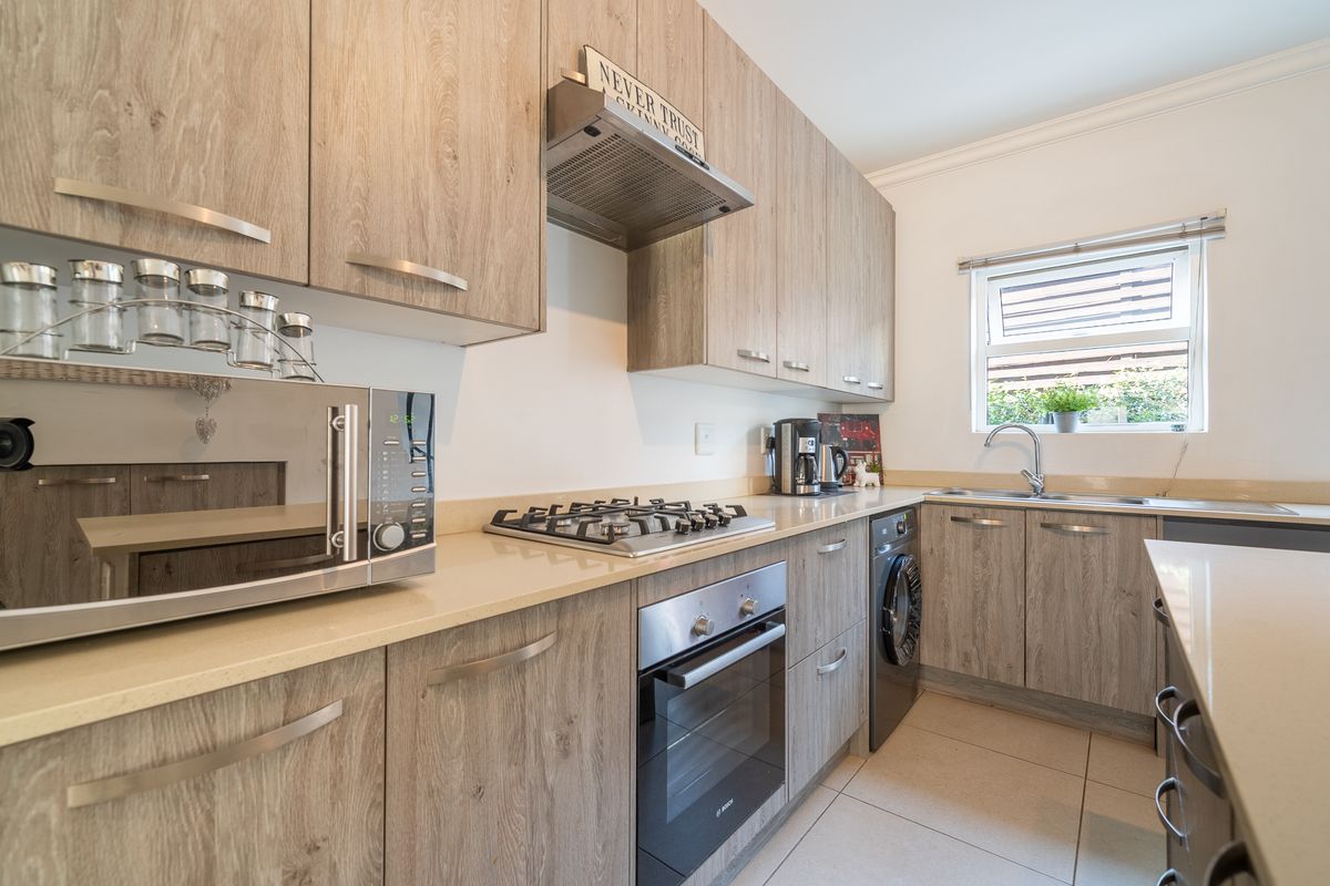 Modern kitchen featuring wood-look cabinetry, stone countertops, integrated gas hob, built-in oven, and stainless steel sink with tiled flooring.