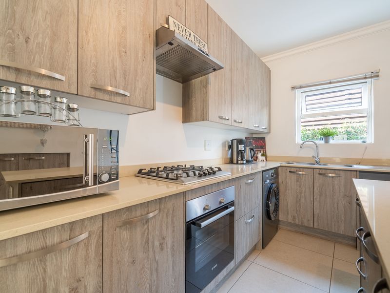 Modern kitchen featuring wood-look cabinetry, stone countertops, integrated gas hob, built-in oven, and stainless steel sink with tiled flooring.