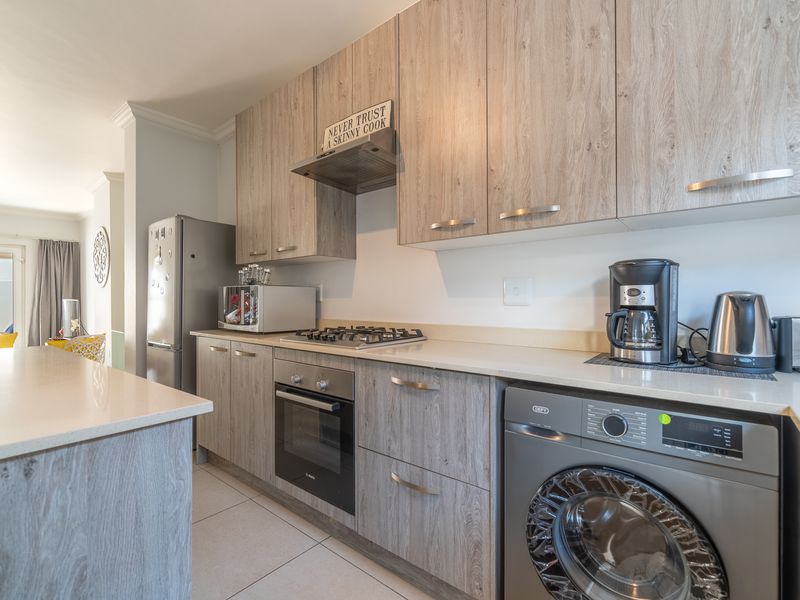 Modern kitchen featuring wood-grain cabinetry, stone countertops, built-in gas hob, oven, extractor fan, and integrated laundry appliance, flowing into an open-plan living area.