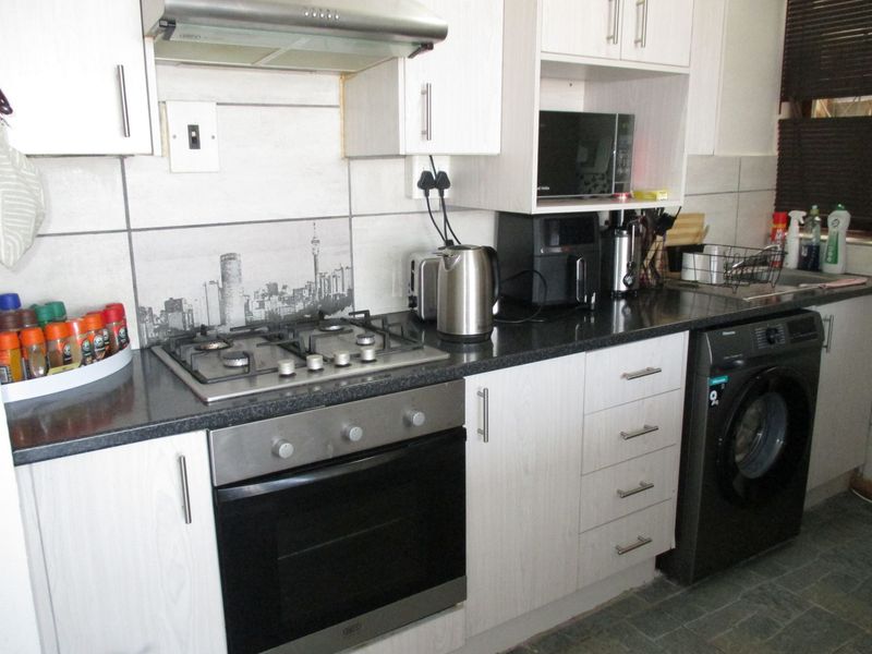 A functional kitchen featuring light wood-look cabinetry, dark stone countertops, a gas hob with extractor fan, and a built-in oven.