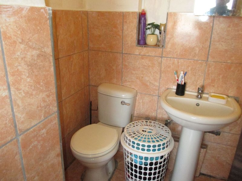 A compact bathroom featuring a pedestal washbasin, toilet, and dated peach-toned wall tiles with a built-in recessed storage niche.
