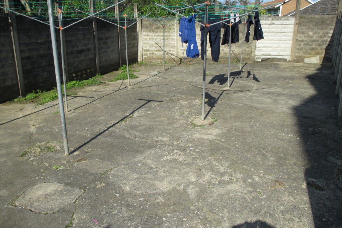 A paved rear courtyard area enclosed by precast concrete boundary walls, featuring multiple rotary washing lines.