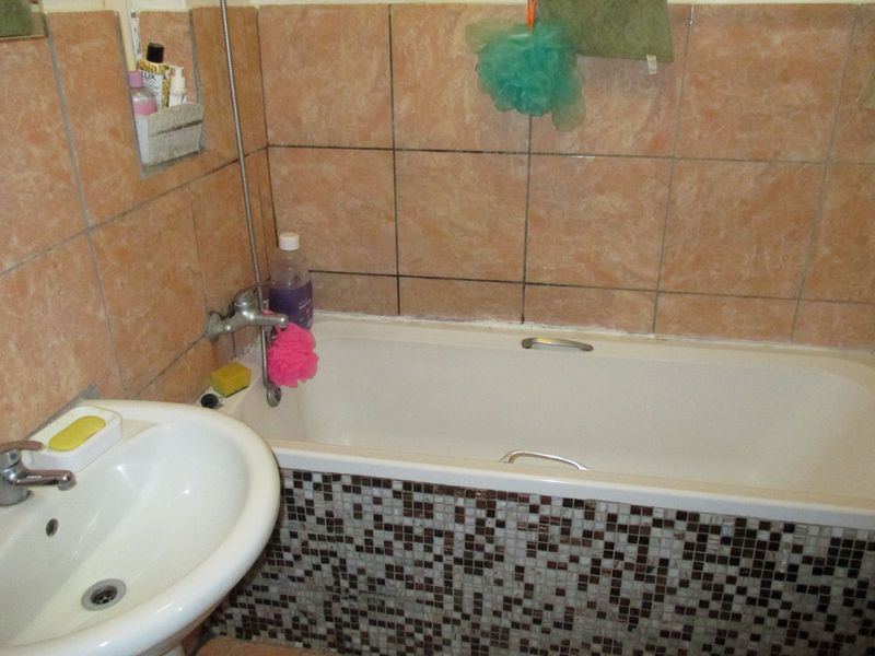 A dated bathroom featuring a bathtub with a mosaic tile apron, pedestal basin, and peach-toned wall tiling.