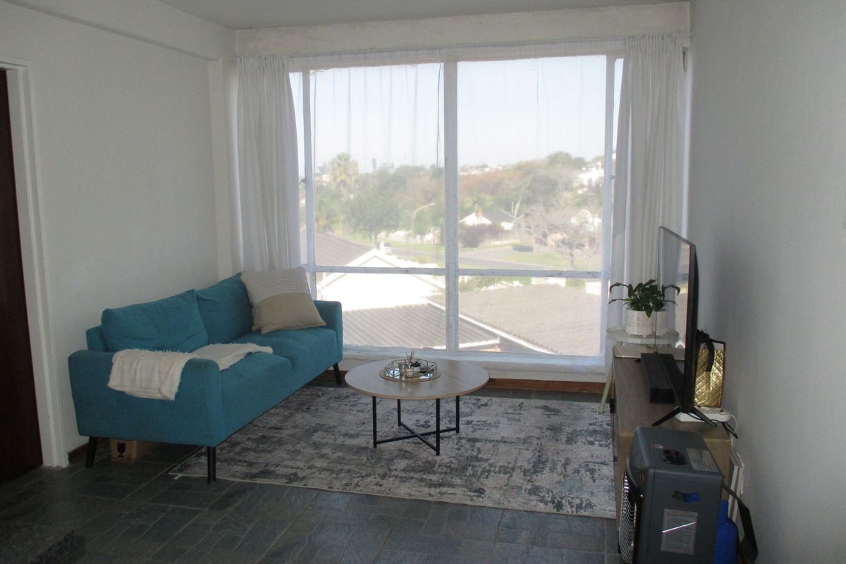 A living room featuring large windows with natural light and stone tile flooring, offering a view of the surrounding neighborhood.