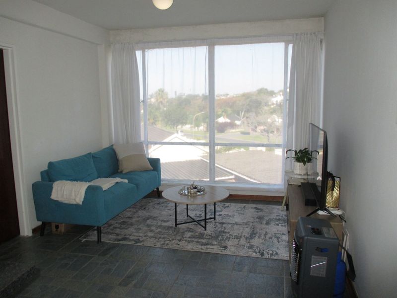 A living room featuring large windows with natural light and stone tile flooring, offering a view of the surrounding neighborhood.