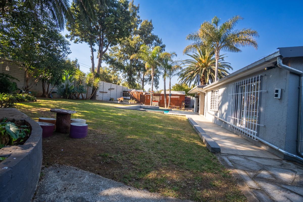 Spacious rear garden featuring a swimming pool, paved walkway, and established trees, providing a private outdoor entertainment area.