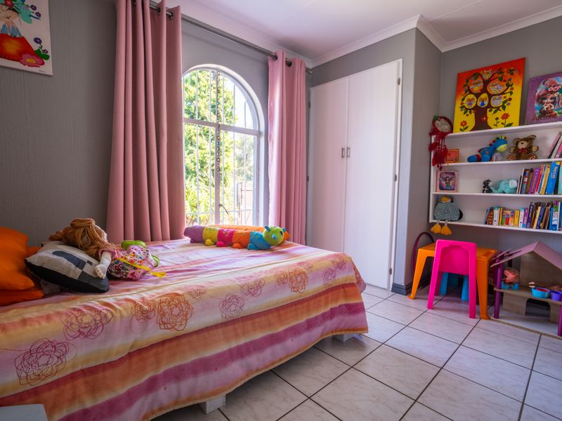 A bright bedroom featuring tiled flooring, a built-in wardrobe, and a distinctive arched window with security bars.