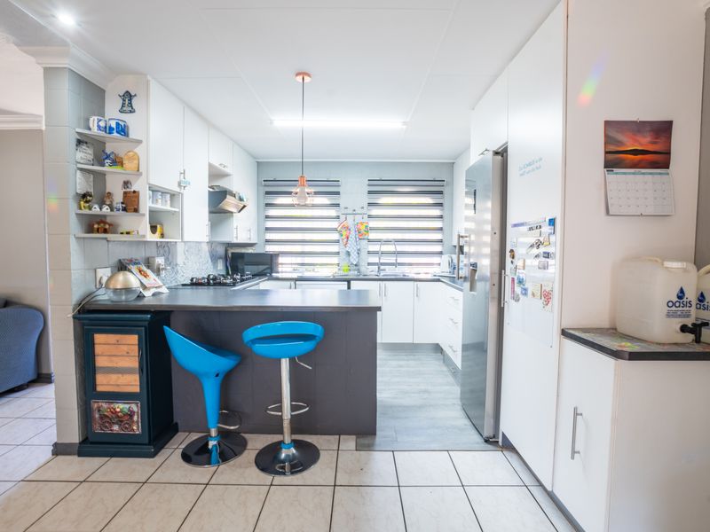 A functional kitchen featuring white cabinetry, dark countertops, a gas hob with extractor, and tiled flooring, offering a clean and practical workspace.