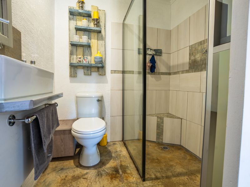 A compact bathroom featuring a walk-in shower with a built-in bench, a modern vessel sink, and a standard toilet with concrete flooring.