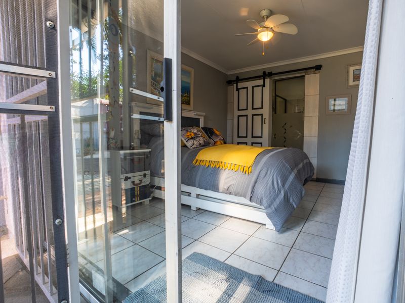 A well-lit bedroom featuring tiled flooring, a ceiling fan, and a sliding barn door providing access to an en-suite bathroom.