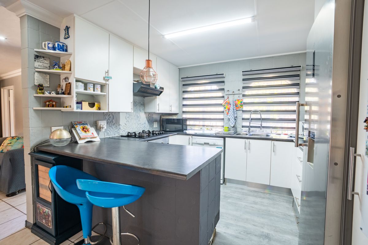 A functional kitchen featuring white cabinetry, dark laminate countertops, a gas hob, and an integrated breakfast bar area with modern finishes.