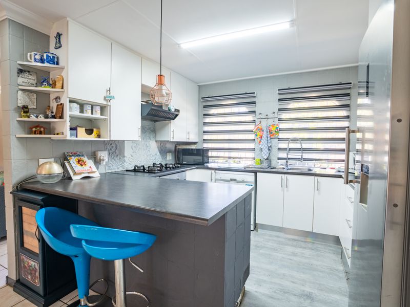 A functional kitchen featuring white cabinetry, dark laminate countertops, a gas hob, and an integrated breakfast bar area with modern finishes.