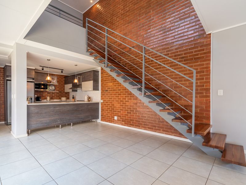 Open-plan living area featuring a striking exposed brick wall, a modern staircase with wooden treads, and a sleek, contemporary kitchen with ample cabinetry.