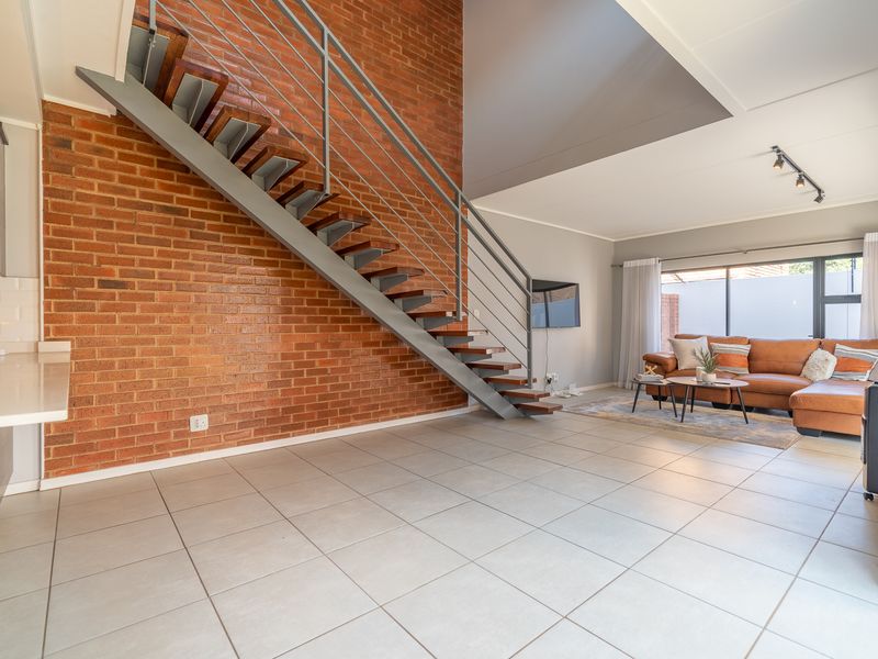 Spacious open-plan living area featuring a striking exposed brick wall, modern metal staircase, and large sliding doors leading to the outdoor space.