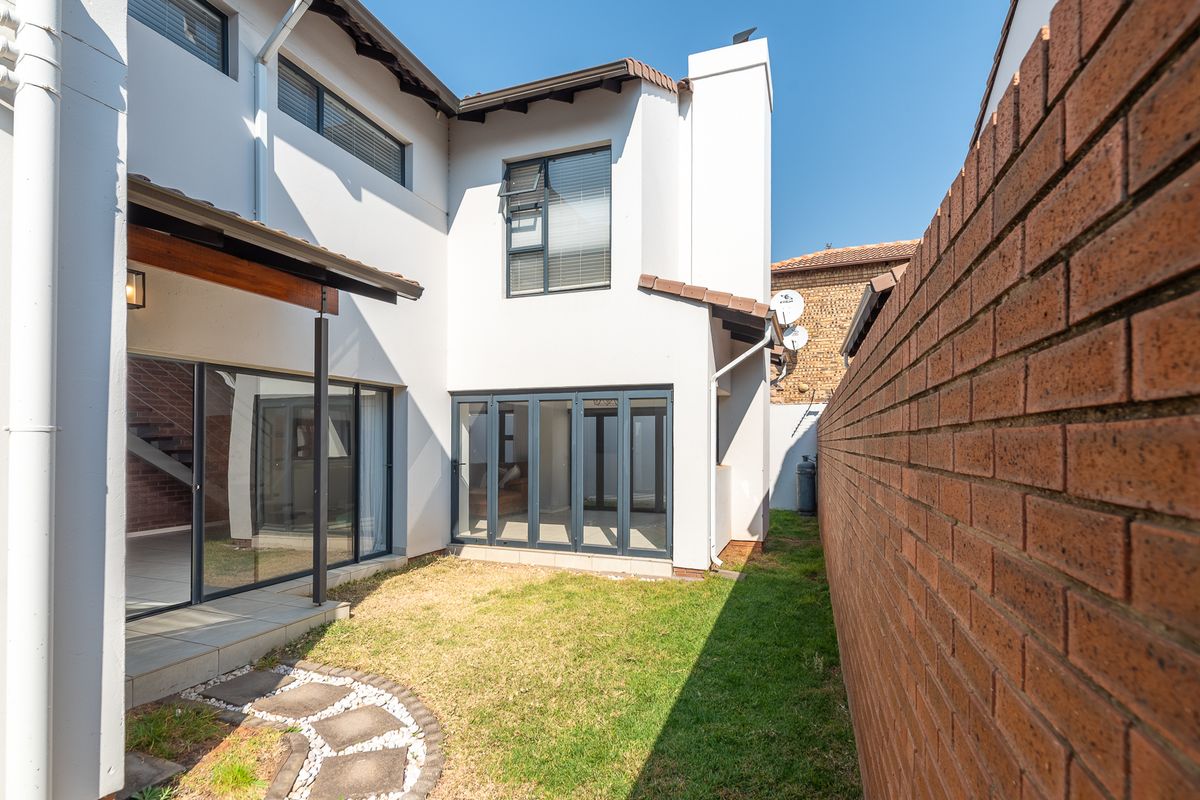 Rear view of the townhouse featuring a small garden, brick boundary wall, tiled patio area with timber pergola, and modern aluminium folding doors.