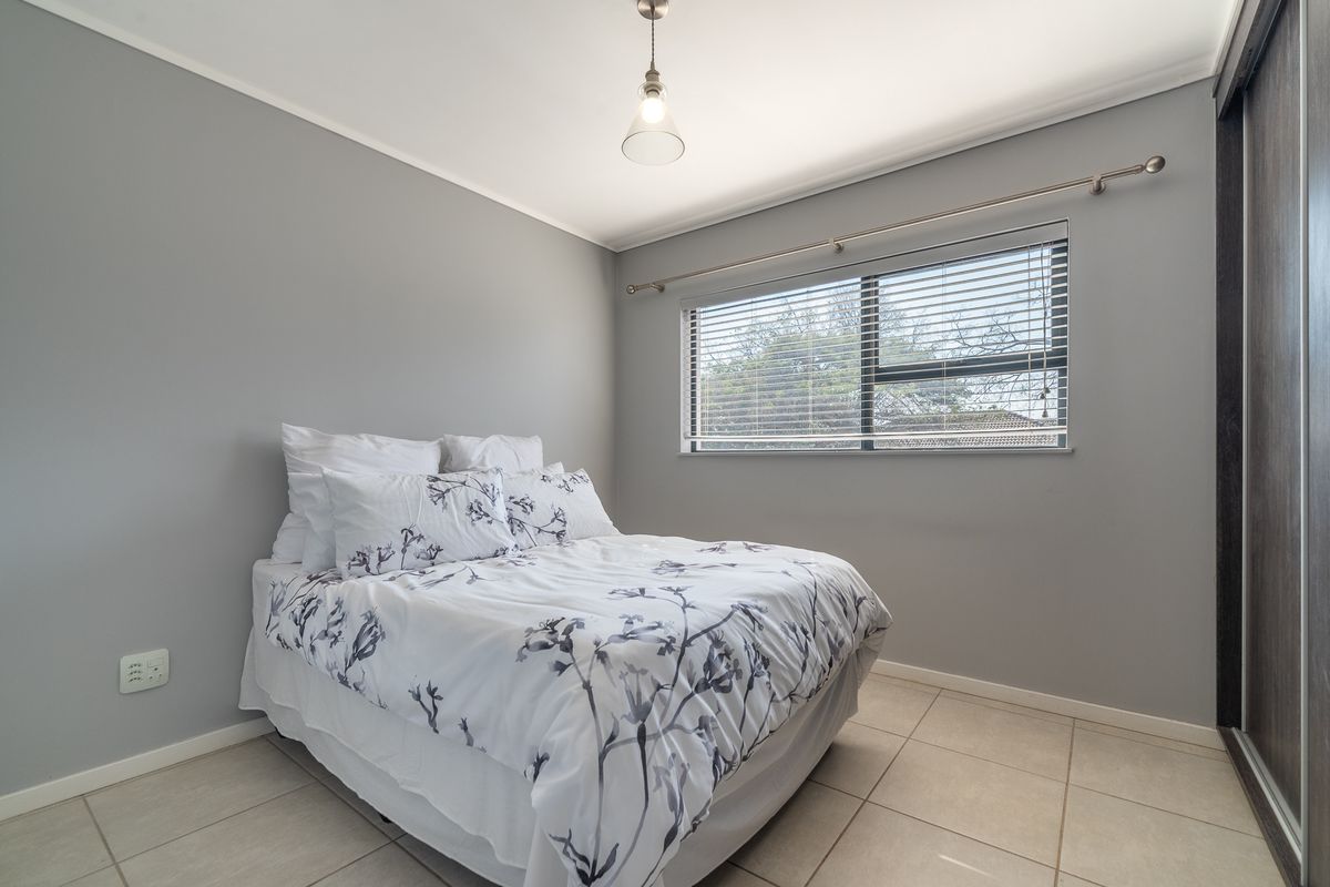 A well-maintained bedroom featuring neutral grey walls, tiled flooring, a built-in wardrobe, and a window fitted with venetian blinds.