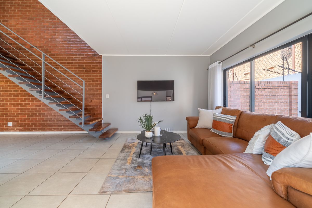 Modern living room featuring an exposed brick feature wall, open-tread staircase with metal balustrade, tiled flooring, and large sliding doors leading to the exterior.