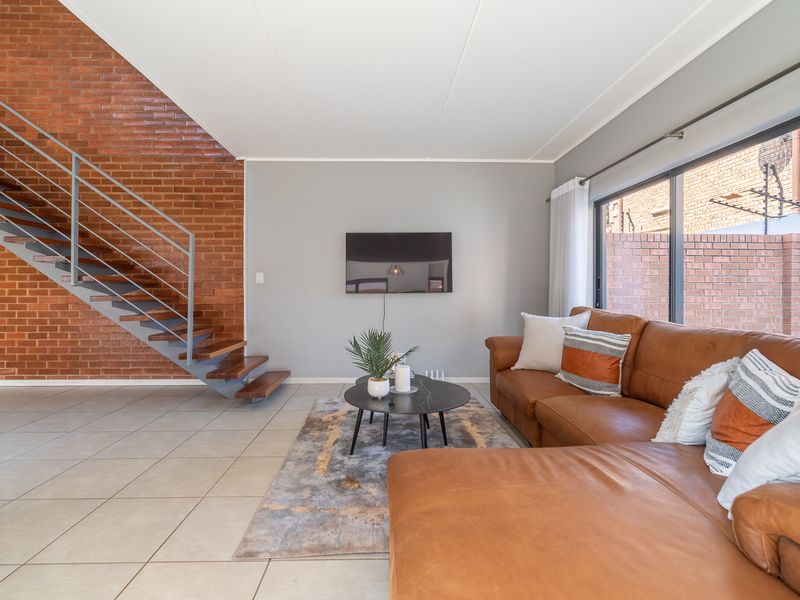 Modern living room featuring an exposed brick feature wall, open-tread staircase with metal balustrade, tiled flooring, and large sliding doors leading to the exterior.