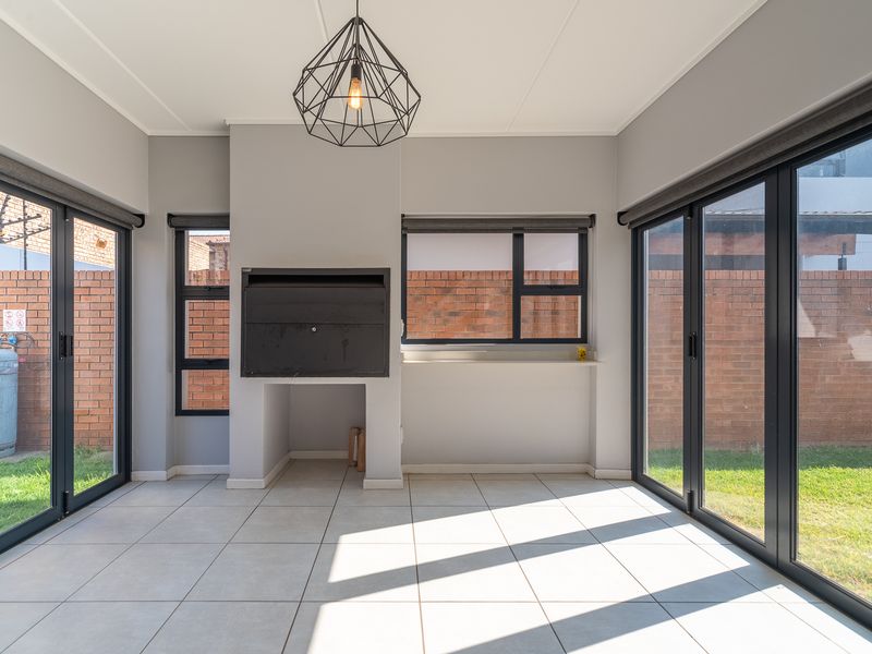 A bright, modern enclosed patio featuring tiled floors, a built-in braai, and large aluminium sliding doors opening to the garden.
