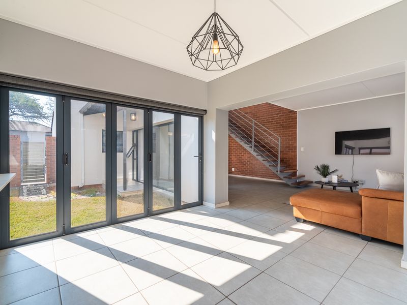 Bright open-plan living area featuring large bi-fold doors opening to the garden, tiled floors, and an exposed brick staircase feature.