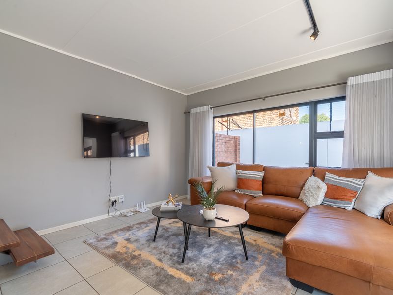 A bright and well-maintained living room featuring neutral grey walls, tiled flooring, and a large window allowing for ample natural light.