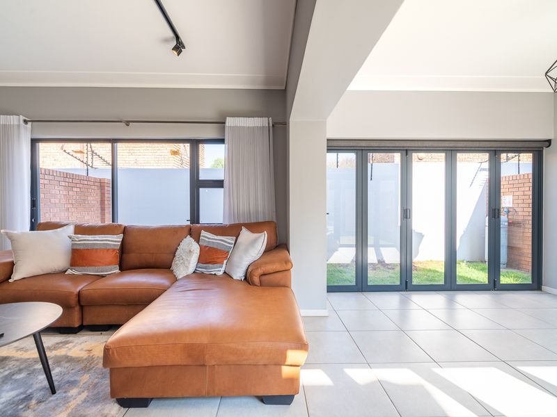 Modern living area featuring large aluminium stacker doors opening to the garden, tiled flooring, and contemporary track lighting.