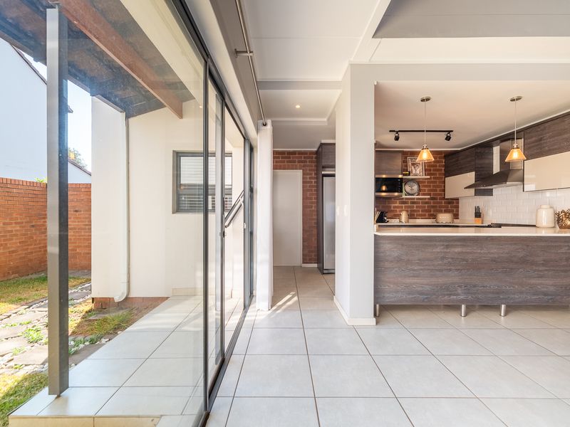 Modern open-plan kitchen and living area featuring sleek cabinetry, stone countertops, subway tile backsplash, and large sliding doors opening to a private garden.