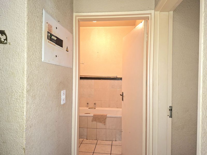A view from a hallway looking into a bathroom featuring a built-in bathtub and tiled finishes, with an electrical distribution board mounted on the wall.
