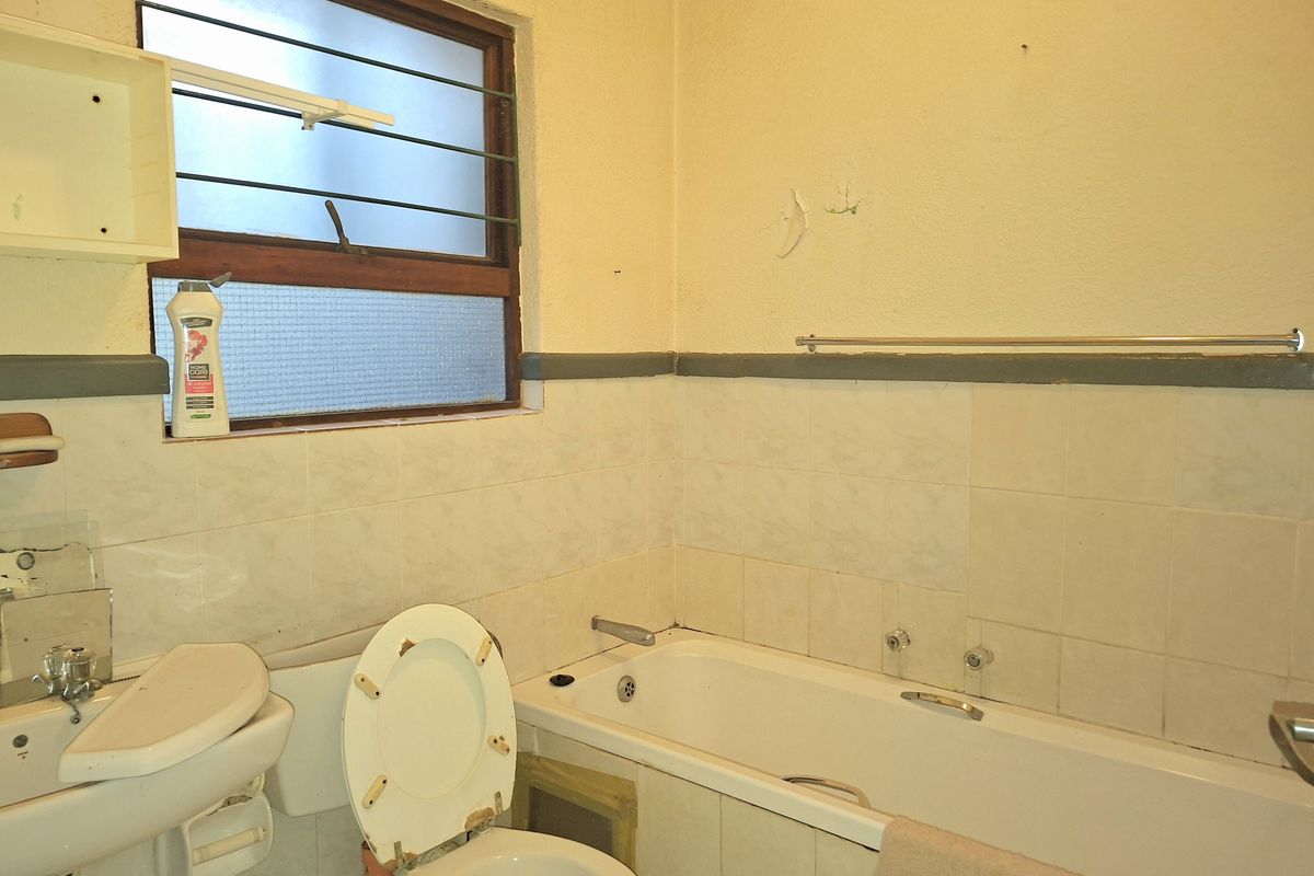 A dated bathroom featuring a standard bathtub, pedestal basin, and toilet, requiring renovation and modernization of fixtures and finishes.